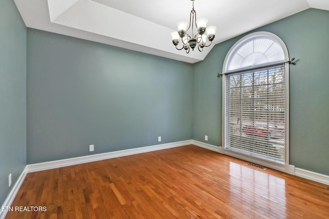 empty room with vaulted ceiling, hardwood / wood-style floors, and a chandelier