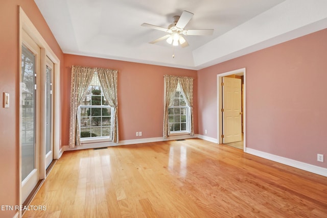 unfurnished room with ceiling fan, a healthy amount of sunlight, a raised ceiling, and light hardwood / wood-style flooring