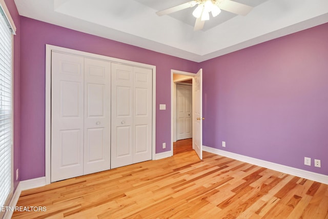 unfurnished bedroom featuring ceiling fan, a raised ceiling, hardwood / wood-style floors, and a closet