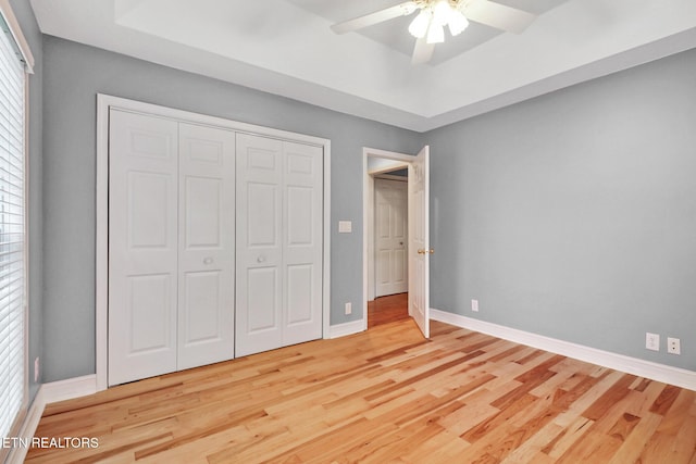 unfurnished bedroom featuring a tray ceiling, a closet, ceiling fan, and hardwood / wood-style flooring