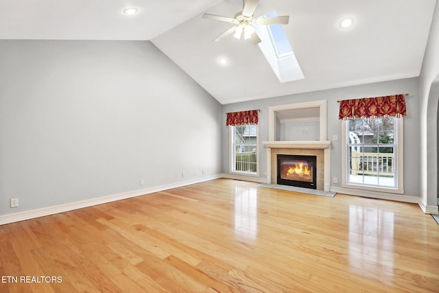 unfurnished living room with a tiled fireplace, lofted ceiling with skylight, and light wood-type flooring