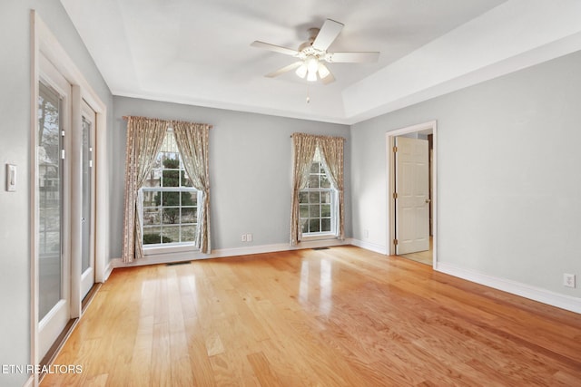 unfurnished room featuring ceiling fan, light wood-type flooring, and a tray ceiling