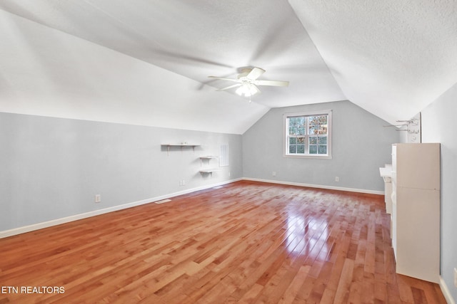 additional living space with ceiling fan, vaulted ceiling, a textured ceiling, and light wood-type flooring