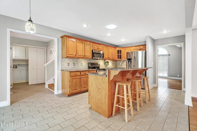 kitchen with a breakfast bar area, stainless steel appliances, light stone counters, an island with sink, and decorative light fixtures