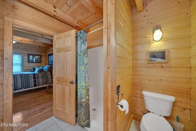 bathroom with a shower with shower curtain, beam ceiling, toilet, and wooden walls