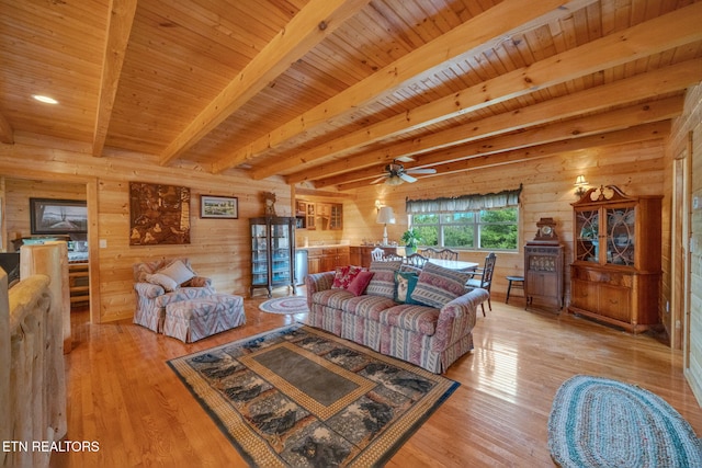 living room with ceiling fan, beam ceiling, wooden walls, and light hardwood / wood-style flooring