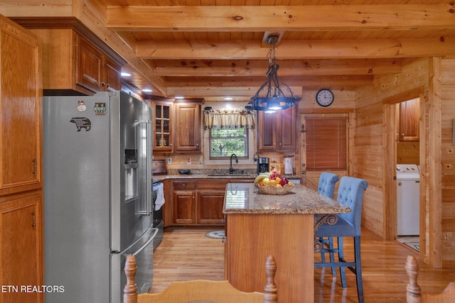 kitchen with pendant lighting, wooden walls, stainless steel fridge, a kitchen island, and washer / dryer