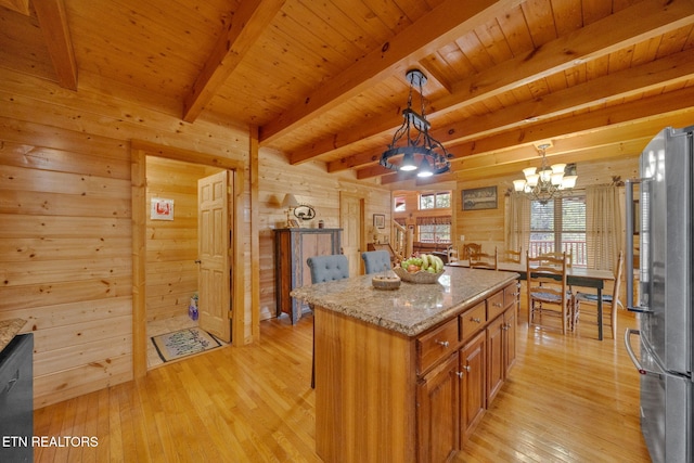 kitchen with light stone countertops, high quality fridge, wooden walls, decorative light fixtures, and a center island