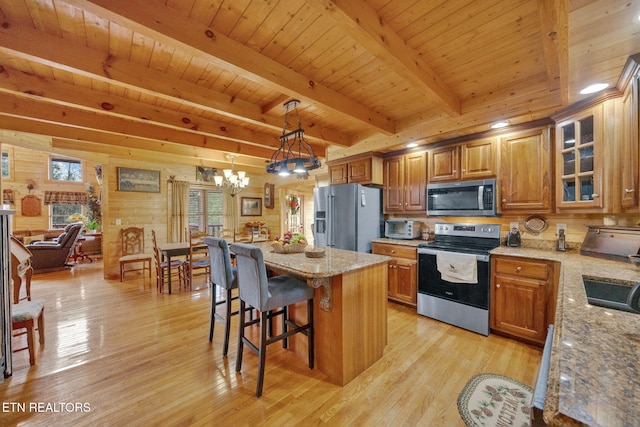 kitchen featuring hanging light fixtures, light stone counters, beamed ceiling, a kitchen island, and appliances with stainless steel finishes