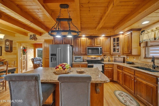 kitchen featuring beam ceiling, sink, hanging light fixtures, stainless steel appliances, and a kitchen island