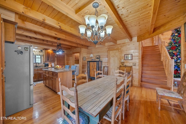 dining space with a chandelier, beam ceiling, light hardwood / wood-style floors, and wood walls