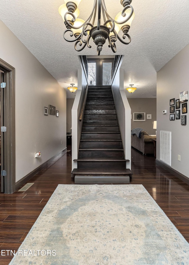 staircase featuring hardwood / wood-style floors, a textured ceiling, and a notable chandelier