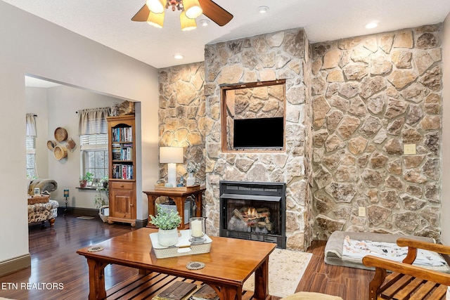 living room with a textured ceiling, a stone fireplace, ceiling fan, and dark hardwood / wood-style floors