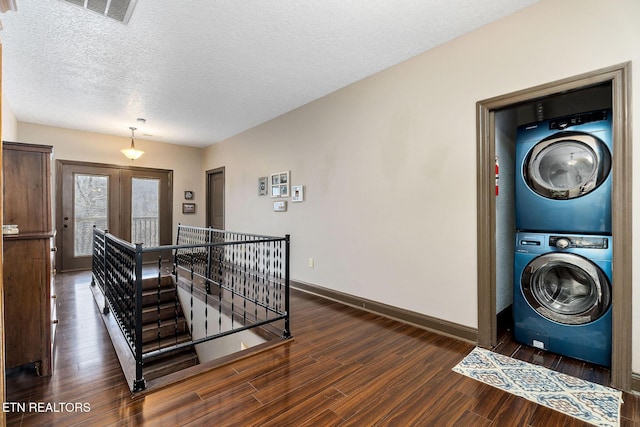 clothes washing area with stacked washer / drying machine, dark hardwood / wood-style floors, a textured ceiling, and french doors