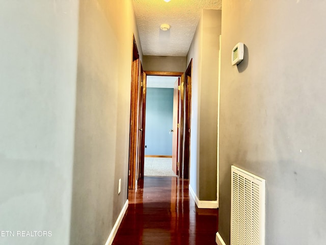 corridor with a textured ceiling and dark wood-type flooring