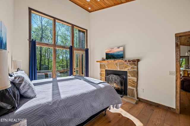 bedroom featuring a fireplace, a towering ceiling, wood ceiling, and wood-type flooring