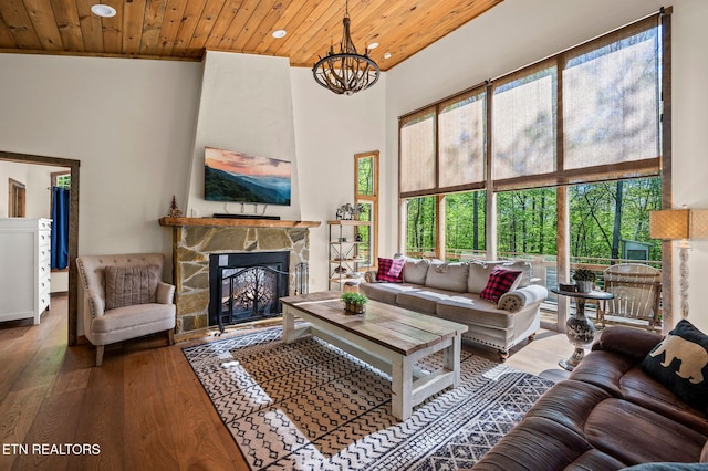 living room featuring hardwood / wood-style floors, wooden ceiling, a stone fireplace, a towering ceiling, and a chandelier