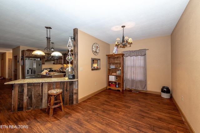 kitchen with dark hardwood / wood-style flooring, a notable chandelier, kitchen peninsula, stainless steel fridge, and a breakfast bar area