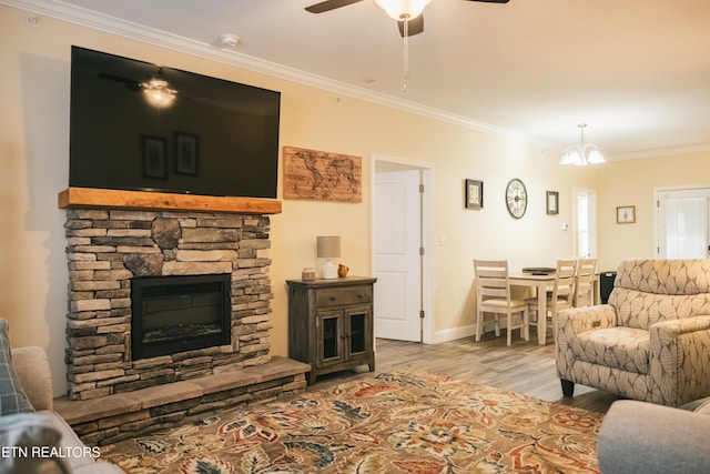 living room with a stone fireplace, light wood-type flooring, ceiling fan with notable chandelier, and ornamental molding