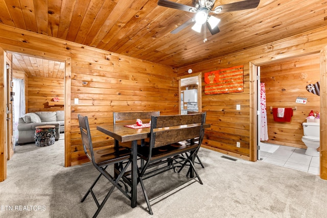 carpeted dining room featuring ceiling fan and wood walls