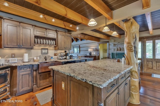 kitchen with beamed ceiling, a center island, hanging light fixtures, and light stone countertops