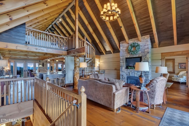 living room featuring hardwood / wood-style floors, high vaulted ceiling, a stone fireplace, wooden walls, and a notable chandelier