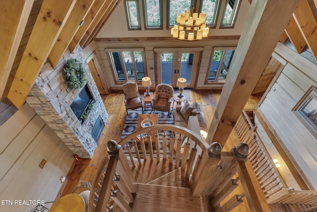 living room with hardwood / wood-style floors, a stone fireplace, wooden walls, a towering ceiling, and a notable chandelier