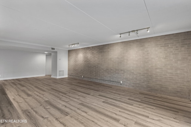 basement with light hardwood / wood-style floors, track lighting, and brick wall