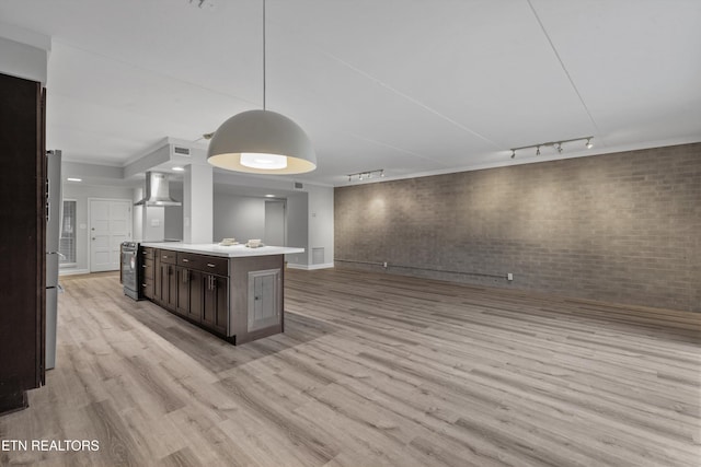 kitchen featuring pendant lighting, a center island, brick wall, wall chimney range hood, and rail lighting