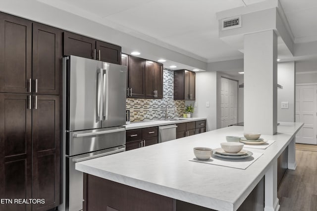 kitchen with ornamental molding, hardwood / wood-style flooring, tasteful backsplash, dark brown cabinetry, and appliances with stainless steel finishes