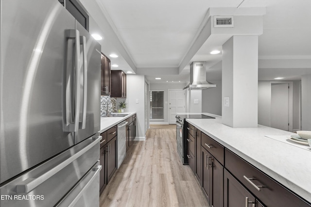 kitchen with wall chimney exhaust hood, stainless steel appliances, light hardwood / wood-style floors, decorative backsplash, and dark brown cabinetry