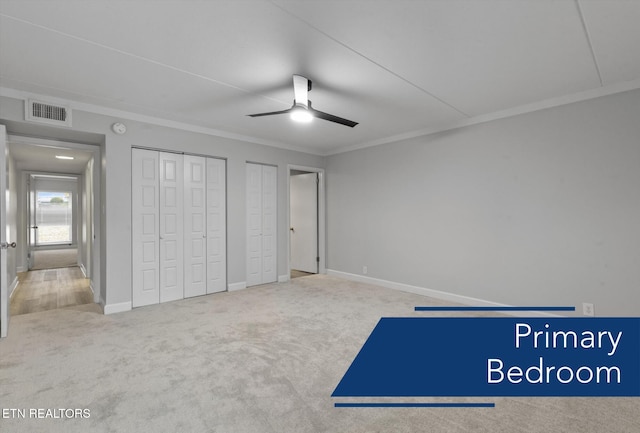 unfurnished bedroom featuring two closets, ornamental molding, carpet floors, and ceiling fan