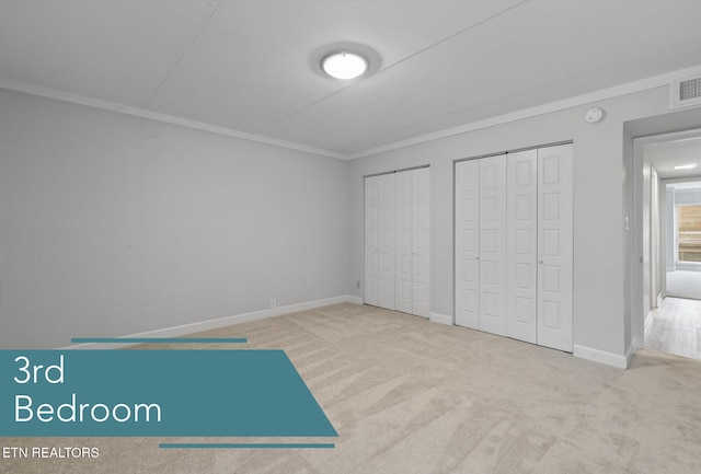 unfurnished bedroom with ornamental molding, multiple closets, and carpet