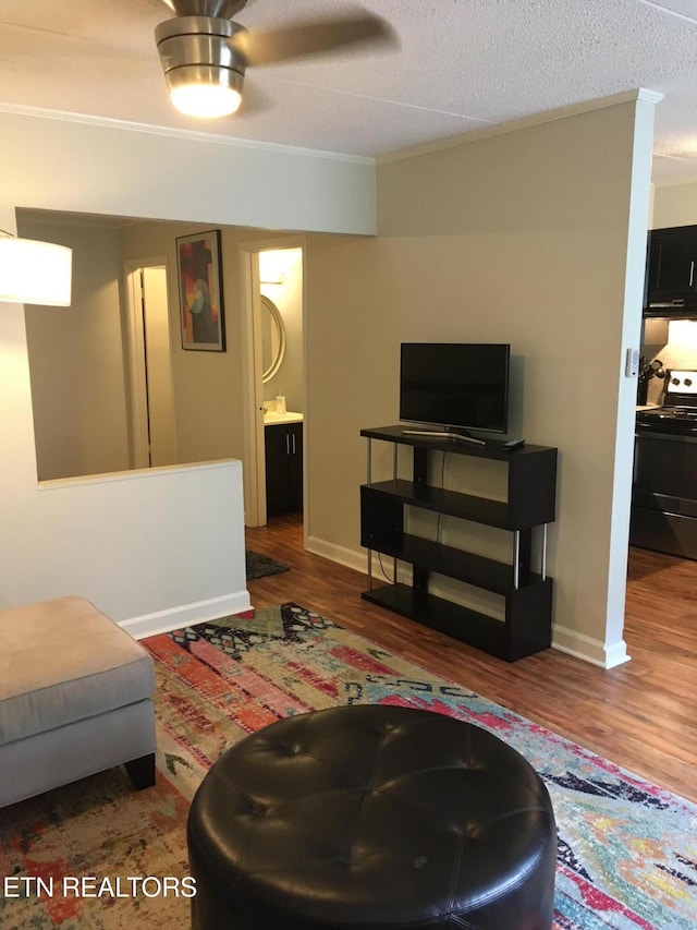 living room featuring ceiling fan, wood-type flooring, a textured ceiling, and ornamental molding