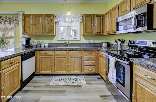 kitchen with decorative light fixtures, stainless steel appliances, a wealth of natural light, brown cabinetry, and a sink