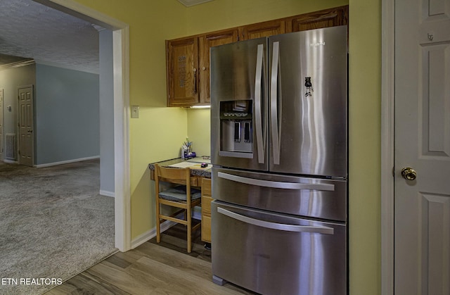 kitchen with a textured ceiling, light wood-style floors, baseboards, brown cabinets, and stainless steel fridge