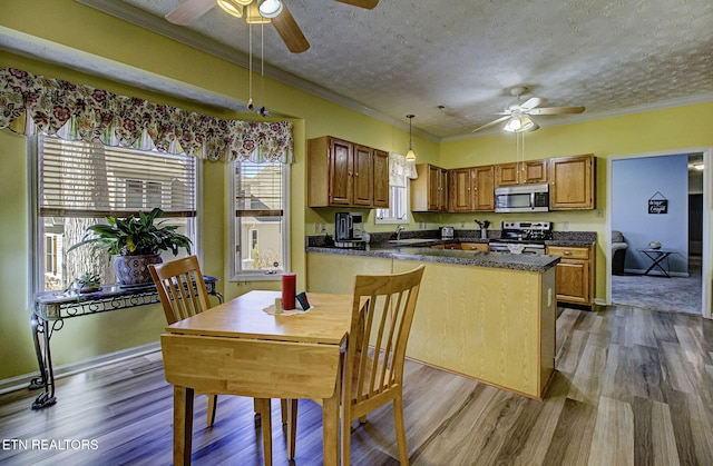 kitchen with brown cabinets, decorative light fixtures, dark countertops, appliances with stainless steel finishes, and ornamental molding