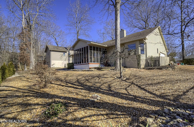 back of house featuring a garage, a sunroom, fence, and a chimney