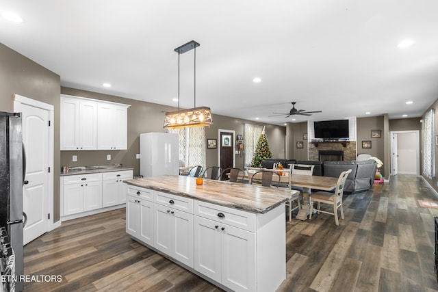 kitchen with white cabinetry, ceiling fan, hanging light fixtures, stainless steel fridge, and a fireplace