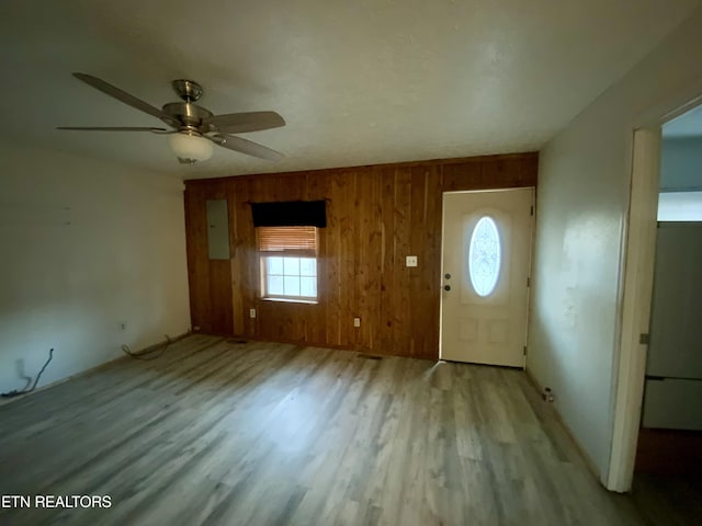 foyer featuring electric panel, light hardwood / wood-style floors, ceiling fan, and wood walls