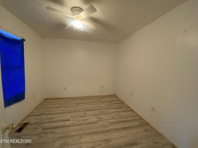 unfurnished room with ceiling fan, a textured ceiling, and light wood-type flooring