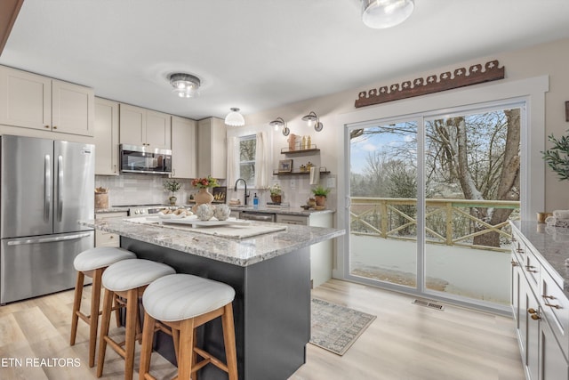 kitchen with appliances with stainless steel finishes, light wood-style flooring, backsplash, and visible vents