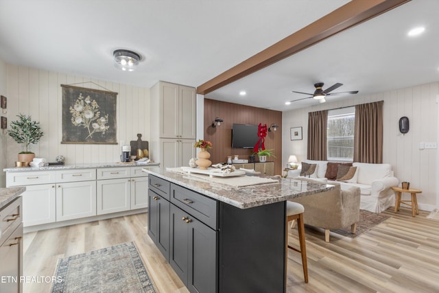 kitchen with ceiling fan, light stone counters, open floor plan, light wood-style floors, and a kitchen bar