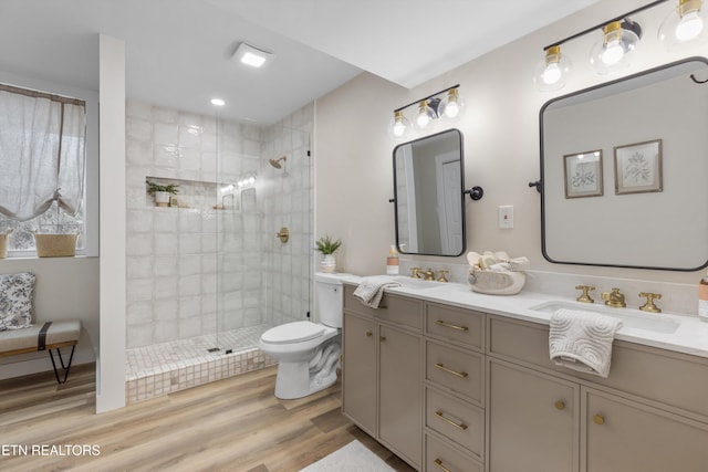 bathroom featuring toilet, wood finished floors, a sink, a tile shower, and double vanity