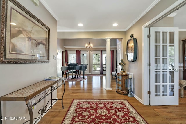 foyer entrance with hardwood / wood-style floors, ornate columns, french doors, a chandelier, and crown molding