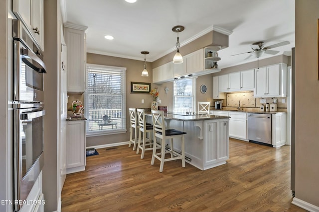 kitchen featuring white cabinets, appliances with stainless steel finishes, decorative light fixtures, a kitchen breakfast bar, and kitchen peninsula