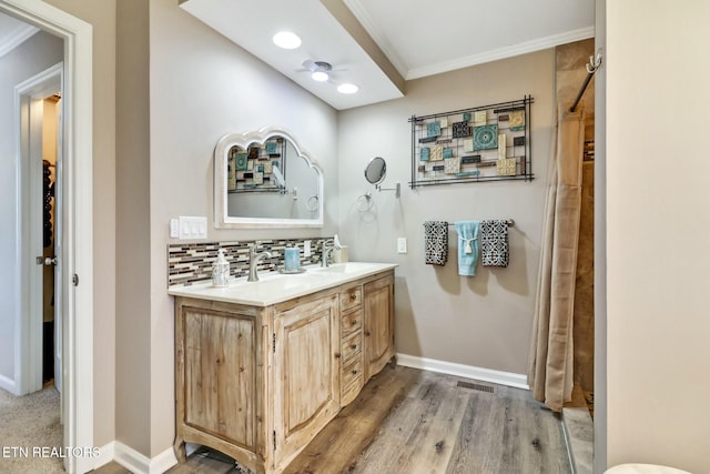 bathroom with wood-type flooring, crown molding, ceiling fan, backsplash, and vanity