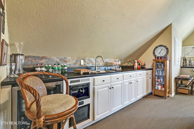 kitchen featuring carpet floors, sink, white cabinets, and vaulted ceiling