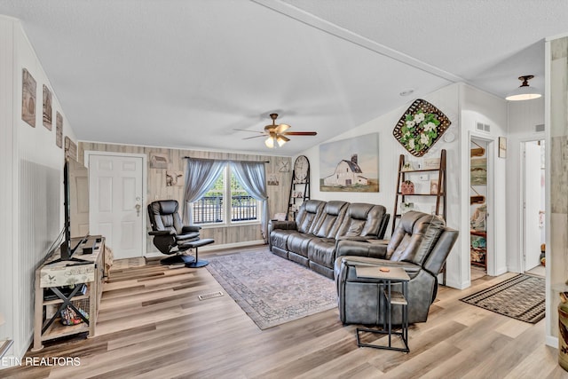 living room featuring ceiling fan, a textured ceiling, light hardwood / wood-style flooring, and wood walls