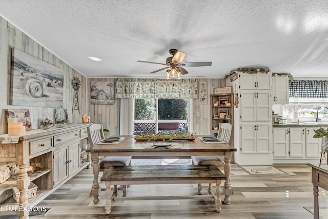 dining area with ceiling fan, wooden walls, a textured ceiling, and light hardwood / wood-style flooring